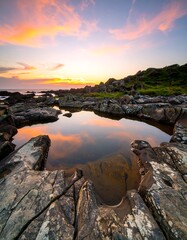 Rocky shoreline at sunset, vibrant colors reflected in a pool