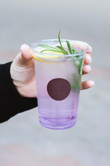 Female hand holding a beautiful purple gradient cocktail or lemonade with fresh rosemary garnish in clear glass.