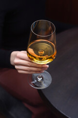 Close-up of a woman's hand holding a glass of white wine in a warm atmosphere.