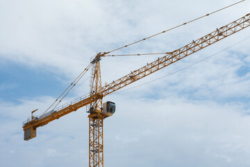 Low angle view of yellow construction tower crane boom extending horizontally against overcast sky. Heavy lifting equipment and machinery used for high-rise building.