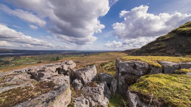 Time lapse of rural landscape with foreground of rocks and grass on hillside and lake in the distance on a spring sunny cloudy day in Arigna mountains in county Leitrim in Ireland.