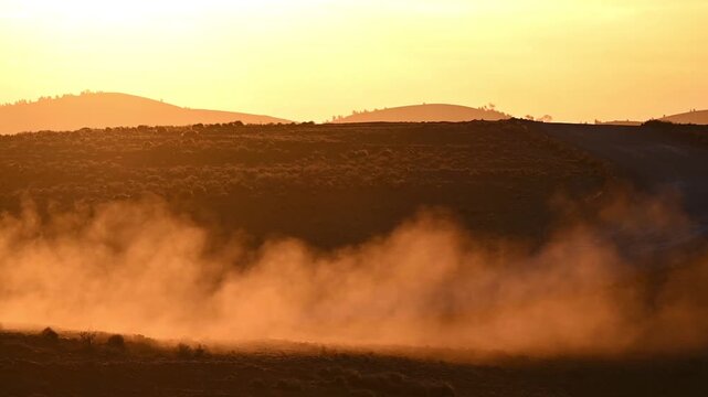 Slowly rising dust from a car driving past during a road trip on the golden sand hills of the outback in Flinders Ranges during sunset in Australia.