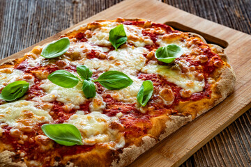 Pinsa Margherita with tomato sauce, basil leaves and mozzarella cheese on wooden background