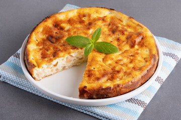 A golden-crusted cottage cheese casserole with a cut-out slice garnished with fresh mint on a woven...