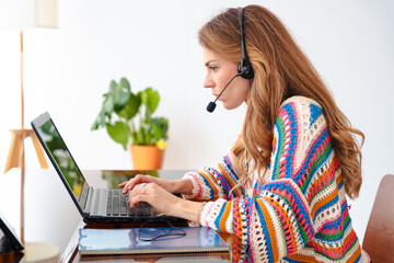 Focused woman with headset and microphone using laptop indoors, remote work, online meeting, customer support, digital communication, freelance job, technology, modern lifestyle, professional activity