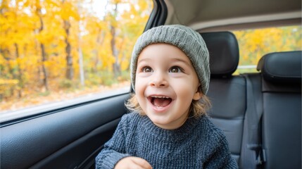 A cheerful child in a car's back seat, mesmerized by the beautiful yellow autumn scenery passing by, wearing a grey beanie and sweater.