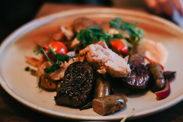 White plate with veal tenderloin, boneless chicken thigh, wagyu and red deer sausage, roasted potatoes, and romesco.