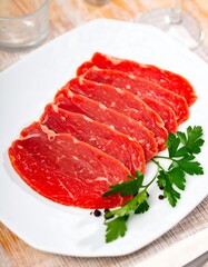 Sliced raw beef on a plate with parsley and peppercorns