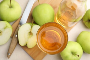 Fresh cider in glass, bottle, apples and knife on beige table, flat lay