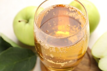 Fresh cider in glass and apples on beige table, closeup