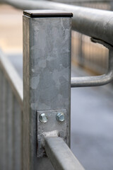 Close up of galvanized steel post with bolts and welded joint on outdoor metal handrail construction. Strong industrial architecture, corrosion protection and durable engineering detail