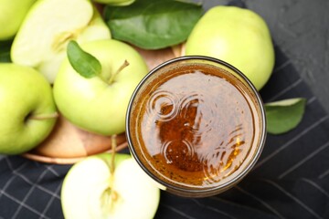 Fresh cider in glass and apples on black table, flat lay