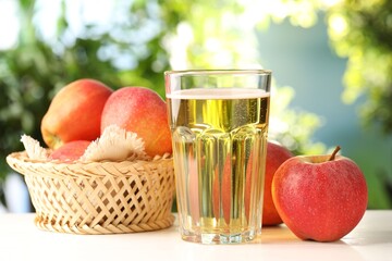 Delicious cider in glass and apples on white wooden table outdoors