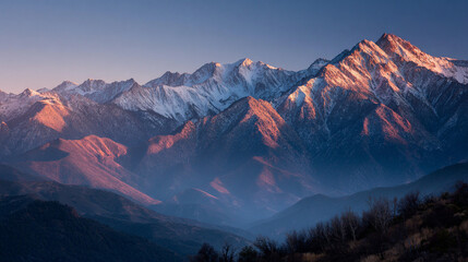 Fototapeta premium A scenic view of snow capped mountains bathed in the warm glow of the setting sun with a clear blue sky