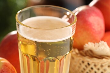 Delicious cider in glass and apples on blurred background, closeup