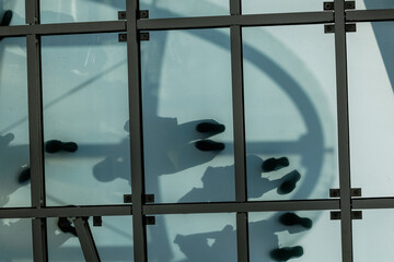 Five shadows show on opaque deck. Sunlight silhouettes indistinct figures of people enjoying elevated observation deck, creating distinct foot patterns attached to soft outlines on teal green glass.