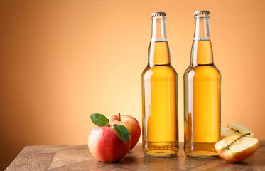Delicious cider in glass bottles and apples on wooden table against orange gradient background, space for text