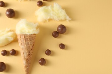 Waffle cone with cotton candy and chocolate sweets on beige background, flat lay. Space for text