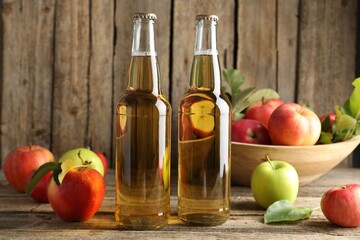 Delicious cider in glass bottles and apples on wooden table