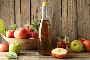 Delicious cider in bottle, glass and apples on wooden table