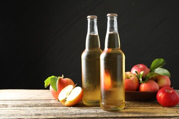 Delicious cider in glass bottles and apples on wooden table against dark gray background. Space for text
