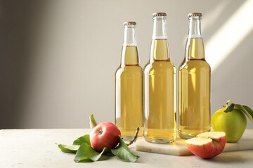 Delicious cider in glass bottles and apples on gray table against light background. Space for text