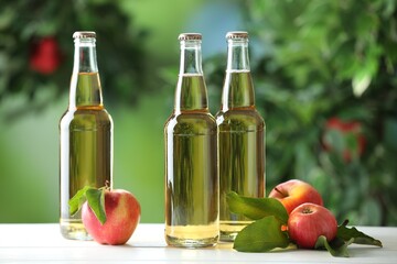 Delicious cider in glass bottles and apples on white wooden table outdoors