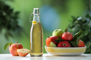 Delicious cider in glass bottle and apples on white wooden table outdoors