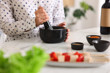 Woman with mortar cooking at table indoors, closeup