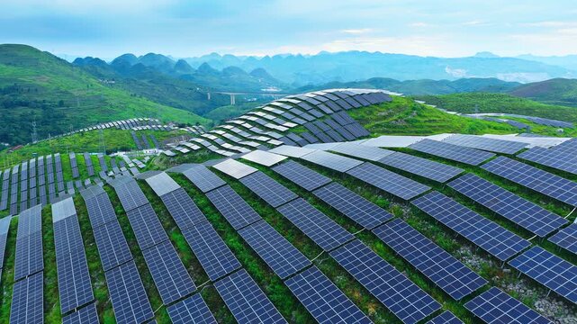 Aerial shot of a large solar power station with countless panels covering green hills.