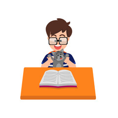 A boy with glasses reading a book at his desk with a cat sitting on his body