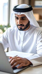 Focused Emirati businessman working on laptop in a modern office setting.