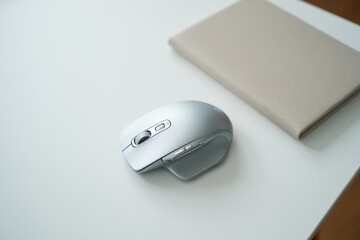 Modern Silver Wireless Mouse and Beige Notebook on White Desk: Minimalist Office Setup