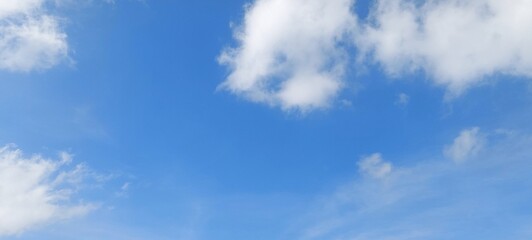 Fototapeta premium Panorama of clear blue sky with fluffy white clouds in clear weather. Panoramic view of blue sky and white clouds on a sunny day. Nature panorama.
