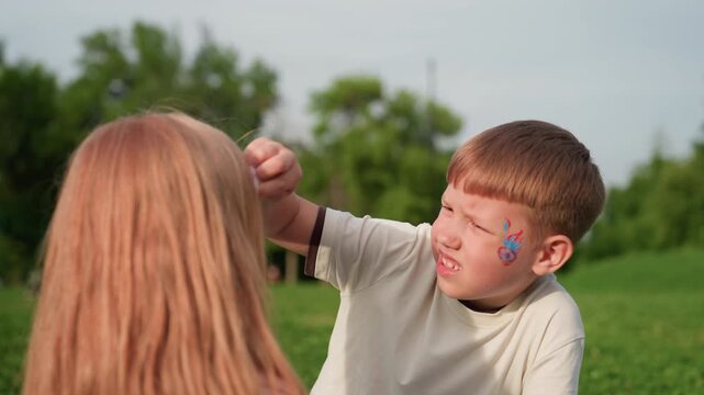 teenager boy gently wiping playmate face with white handkerchief in grassy park during warm light, showing care and friendship between youth, soft background blur emphasizing tender moment of support