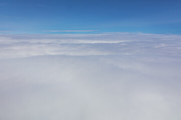 High altitude aerial photograph of fluffy white clouds and blue sky taken from an airplane window