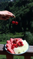 Young Woman Holding Cherries on Fruit Plate at Balcony with Scenic View