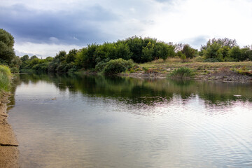 Scenic view of a calm river reflecting surrounding trees and cloudy sky in the countryside