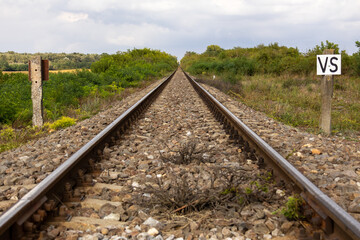 Straight railway tracks running through green countryside vegetation under a cloudy sky