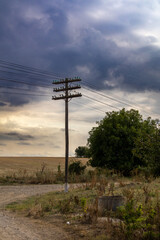 Wooden utility poles with power lines standing in a rural countryside landscape under cloudy sky