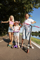 Group of cheerful kids riding scooters outdoors on a sunny day in summer