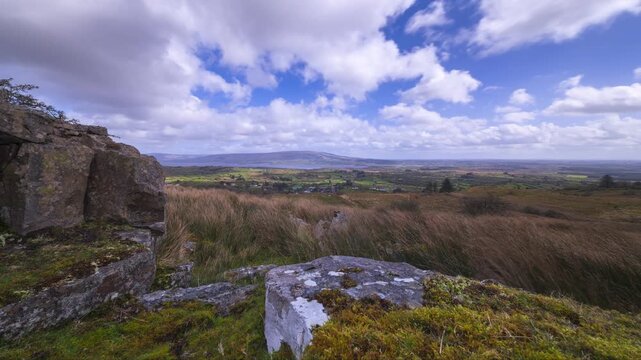 Time lapse of rural landscape with rocky foreground and hills and lake in the distance during a cloudy sunny spring day in Arigna mountains in county Leitrim in Ireland.