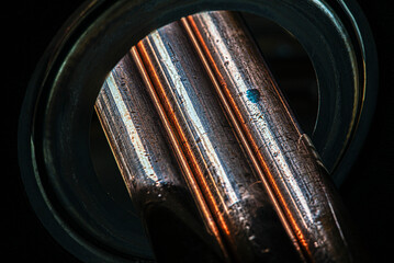 Copper rods with texture in close-up passing through a hole in an industrial space with contrasting light