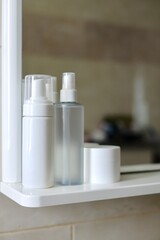 Care products, cosmetics and comb on the shelf in white bathroom. Cleanser, lotion, cream and comb near mirror. White bathroom. Women care products. Yellow comb. 