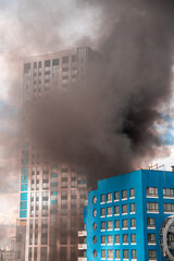 Modern skyscraper is engulfed in flames and emitting a large plume of dark smoke, creating a dramatic scene of destruction in a densely populated urban environment