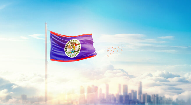 Belize flag wavering in beautiful clouds with building skyline. The flag with drone shot in beautiful sky. Belize national flag for independence day. - Powered by Adobe