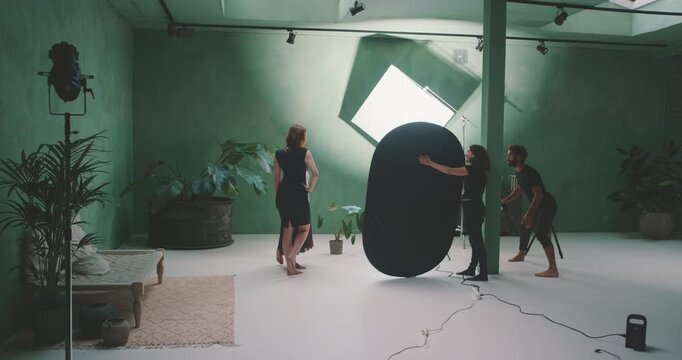 Models posing in green screen studio with photographer and assistant holding reflector