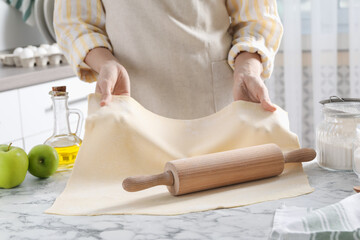 Making delicious apple strudel. Woman shaping dough at white marble table in kitchen, closeup