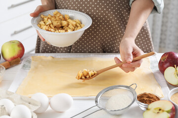 Making delicious apple strudel. Woman putting pieces of fruit onto dough at table in kitchen, closeup