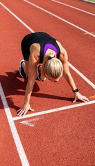 Blonde woman in sprinter&rsquo;s stance ready to run on red track.